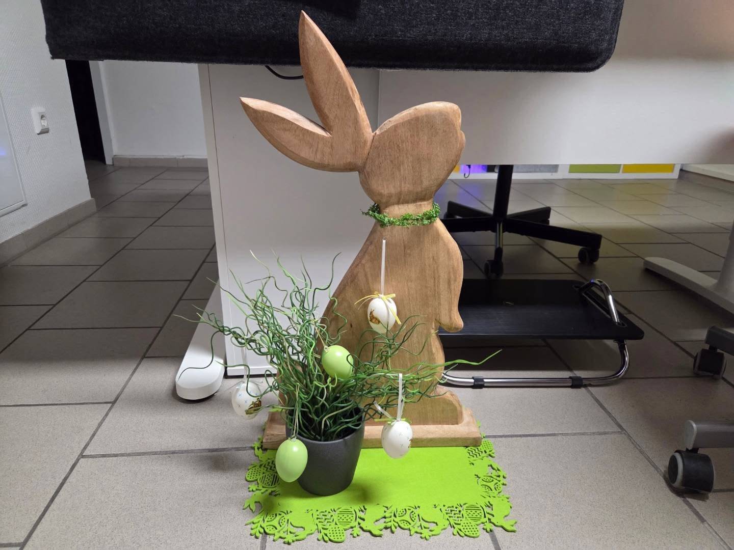 Bürostuhl, Schreibtisch, davor ein Osterhase mit Ostergesteck
