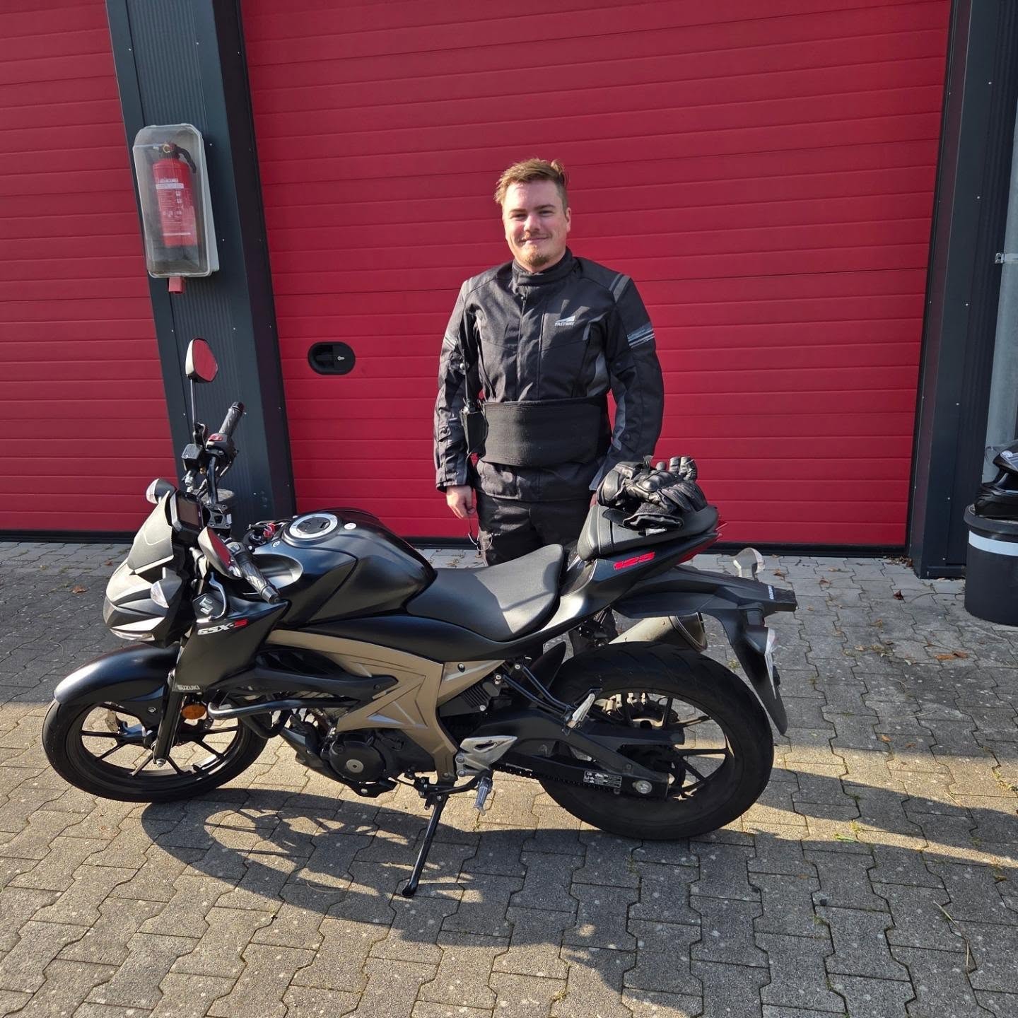 Garagenhof mit roten Toren und dem neuen Führerscheininhaber inkl. Motorrad davor