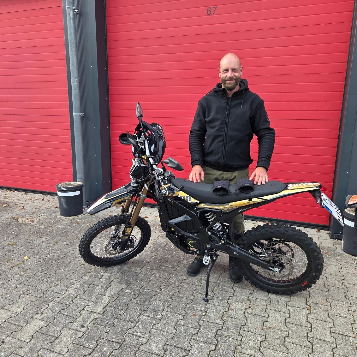 Garagenhof mit roten Toren und dem neuen Führerscheininhaber inkl. Motorrad davor
